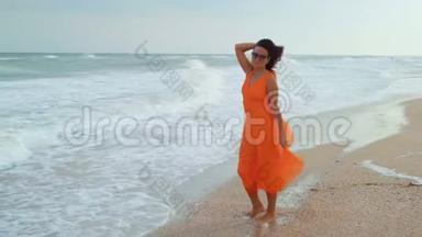 美丽的女人穿着橙色的衣服，戴着太阳镜，<strong>站在</strong>潮湿的沙滩<strong>上</strong>，<strong>站在</strong>大海的背景<strong>上</strong>